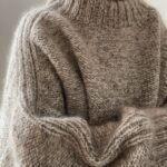 A person wearing a thick, textured beige heavy knit sweater with a high ribbed neckline.