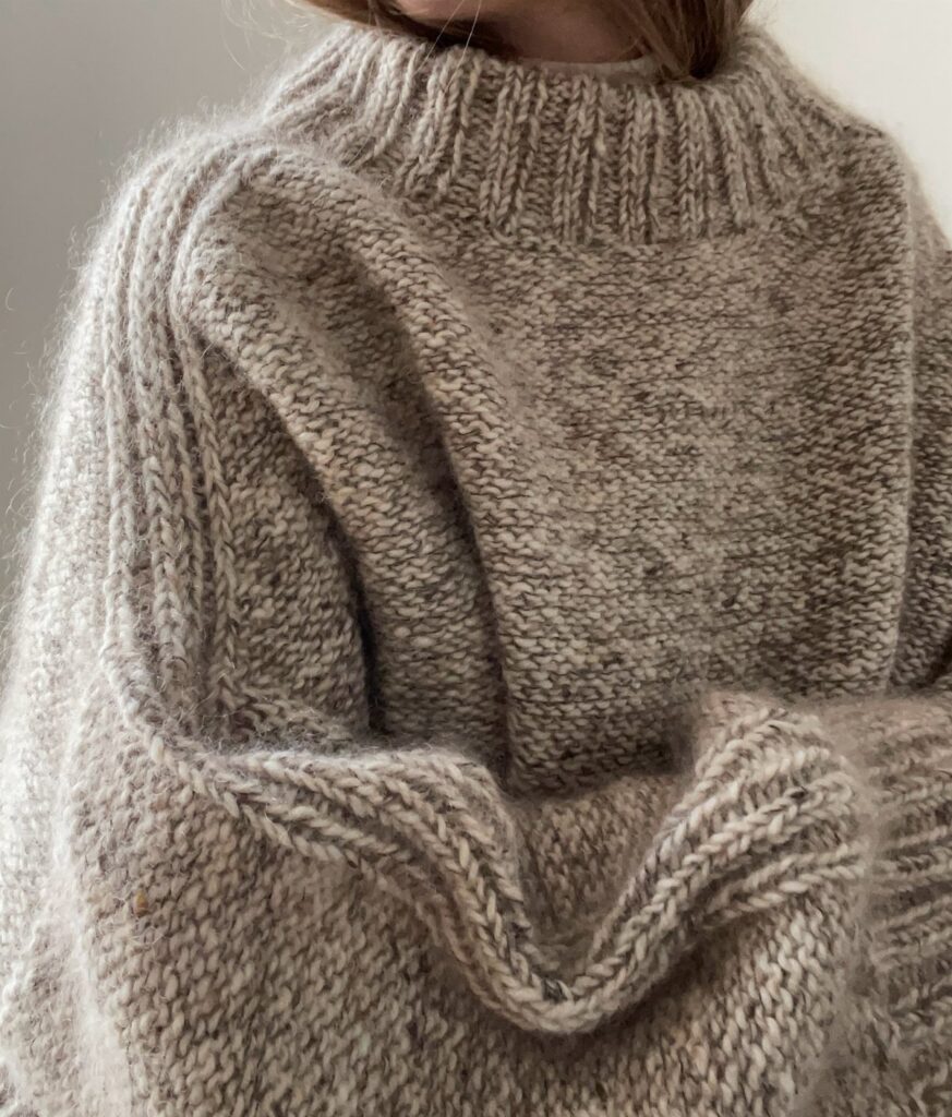 A person wearing a thick, textured beige heavy knit sweater with a high ribbed neckline.