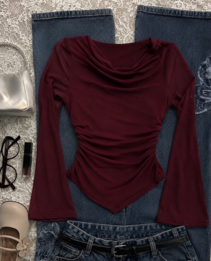 Burgundy long-sleeved cowl neck top with flared sleeves laid on blue denim jeans.