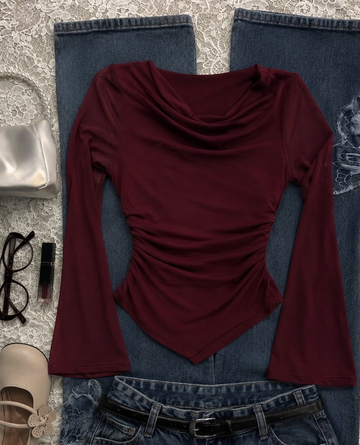 Burgundy long-sleeved cowl neck top with flared sleeves laid on blue denim jeans.
