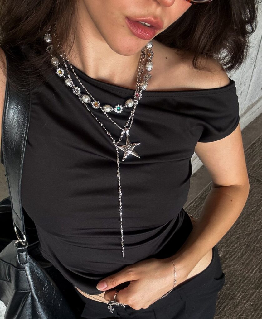 A person wearing a black top adorned with several layered silver necklaces and a star pendant.