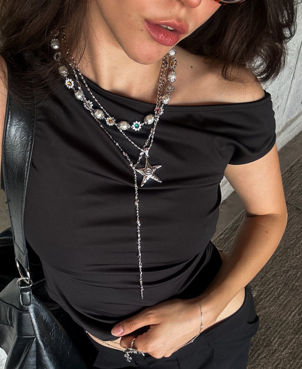 A person wearing a black top adorned with several layered silver necklaces and a star pendant.
