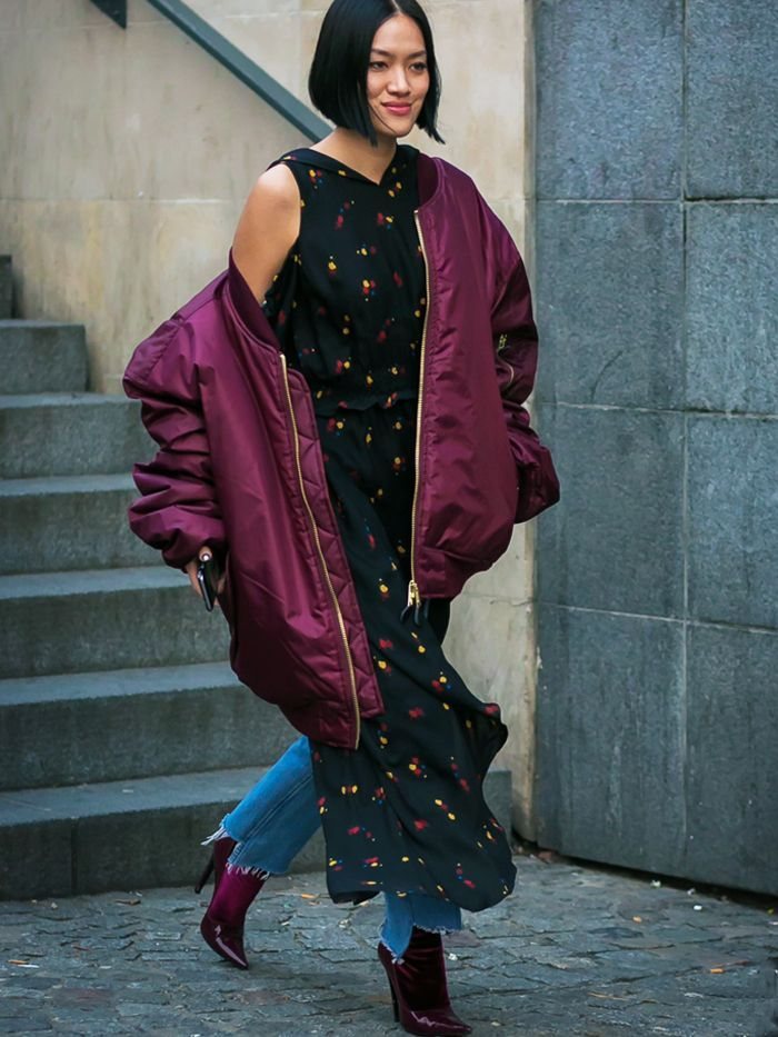 Woman walking in a burgundy bomber jacket over a black floral maxi dress and purple boots.