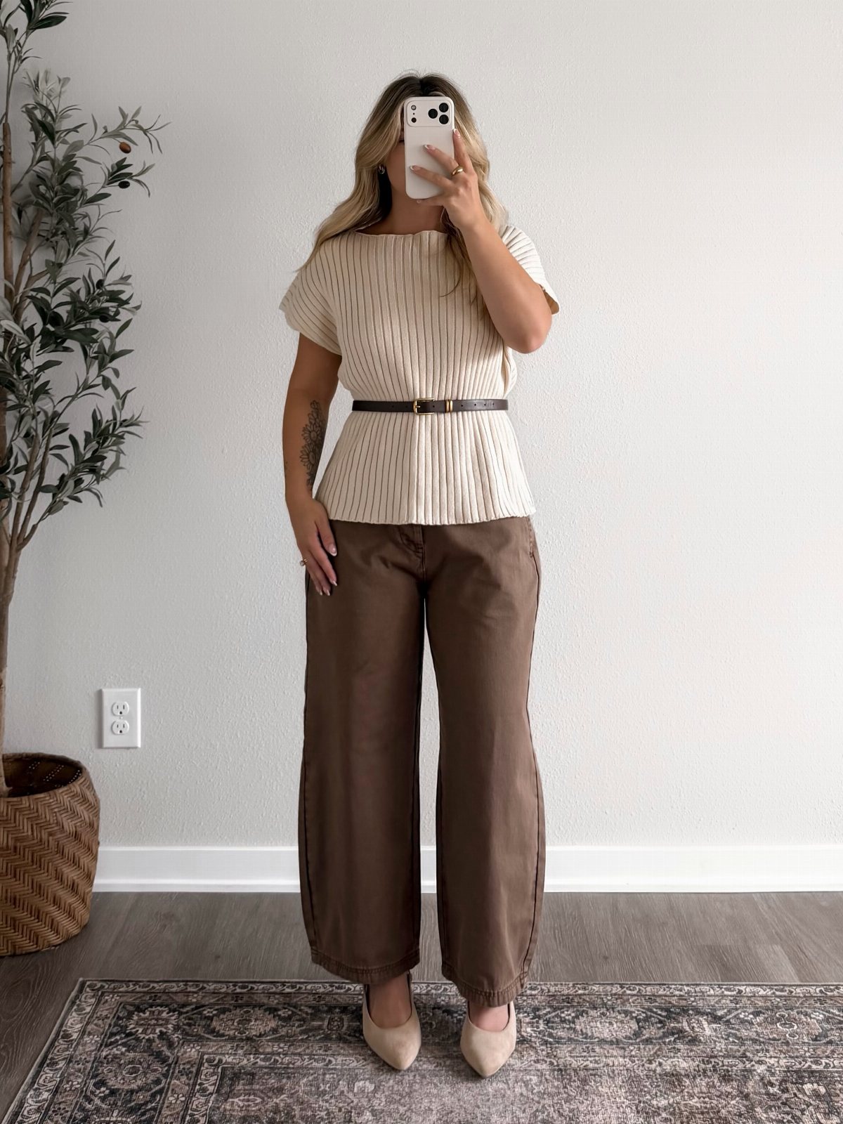 Woman posing in a striped beige top, brown wide-leg trousers, and beige flats.