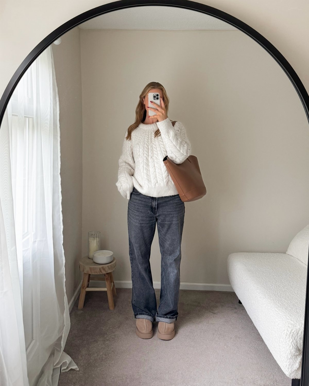 Woman in a white knit sweater and dark jeans posing for a mirror selfie.