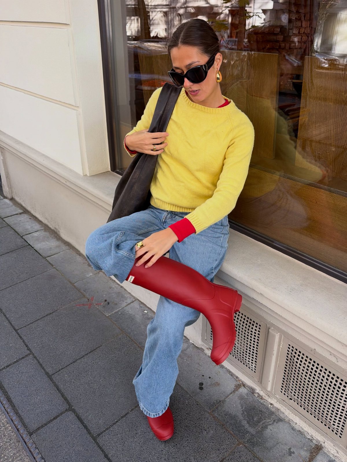 Woman in a yellow sweater and blue jeans wearing bright red rain boots.