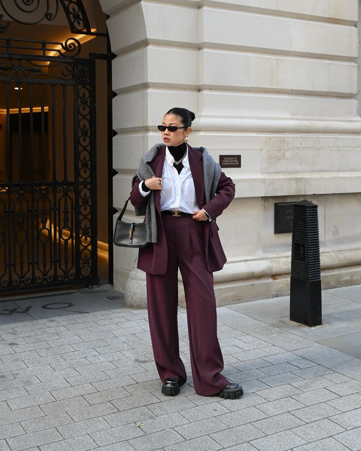 A woman posing in a burgundy pantsuit and white shirt on a city street.