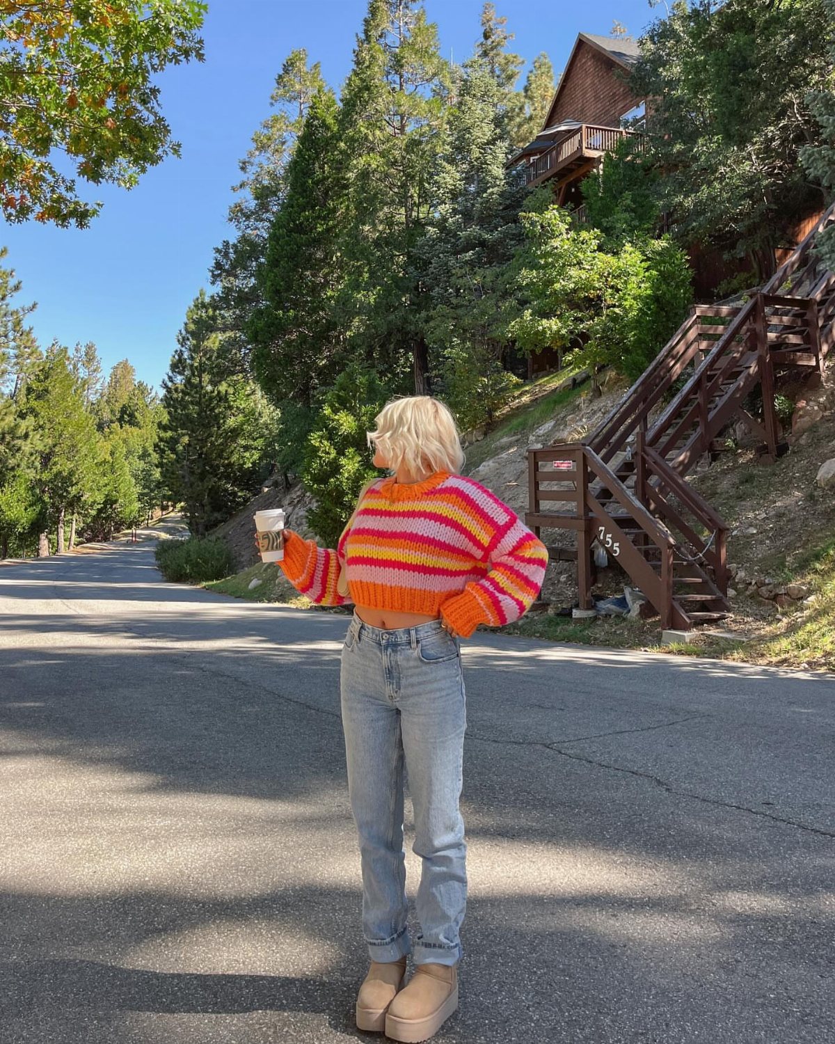 A woman wearing a colorful striped knit sweater and light blue jeans standing on a road.