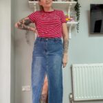 A woman wearing a red striped t-shirt and a long blue denim skirt with a slit.