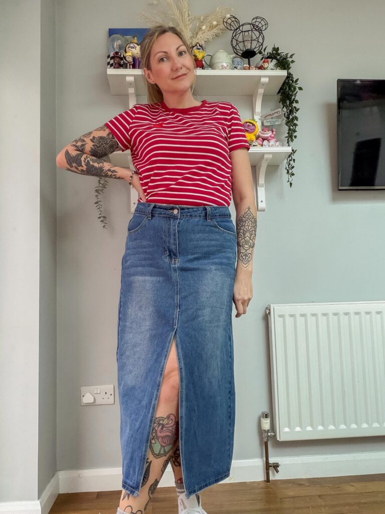 A woman wearing a red striped t-shirt and a long blue denim skirt with a slit.