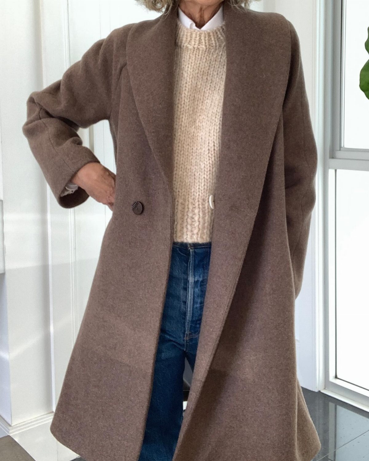 Taupe handmade wool coat worn over a cream sweater and blue jeans.