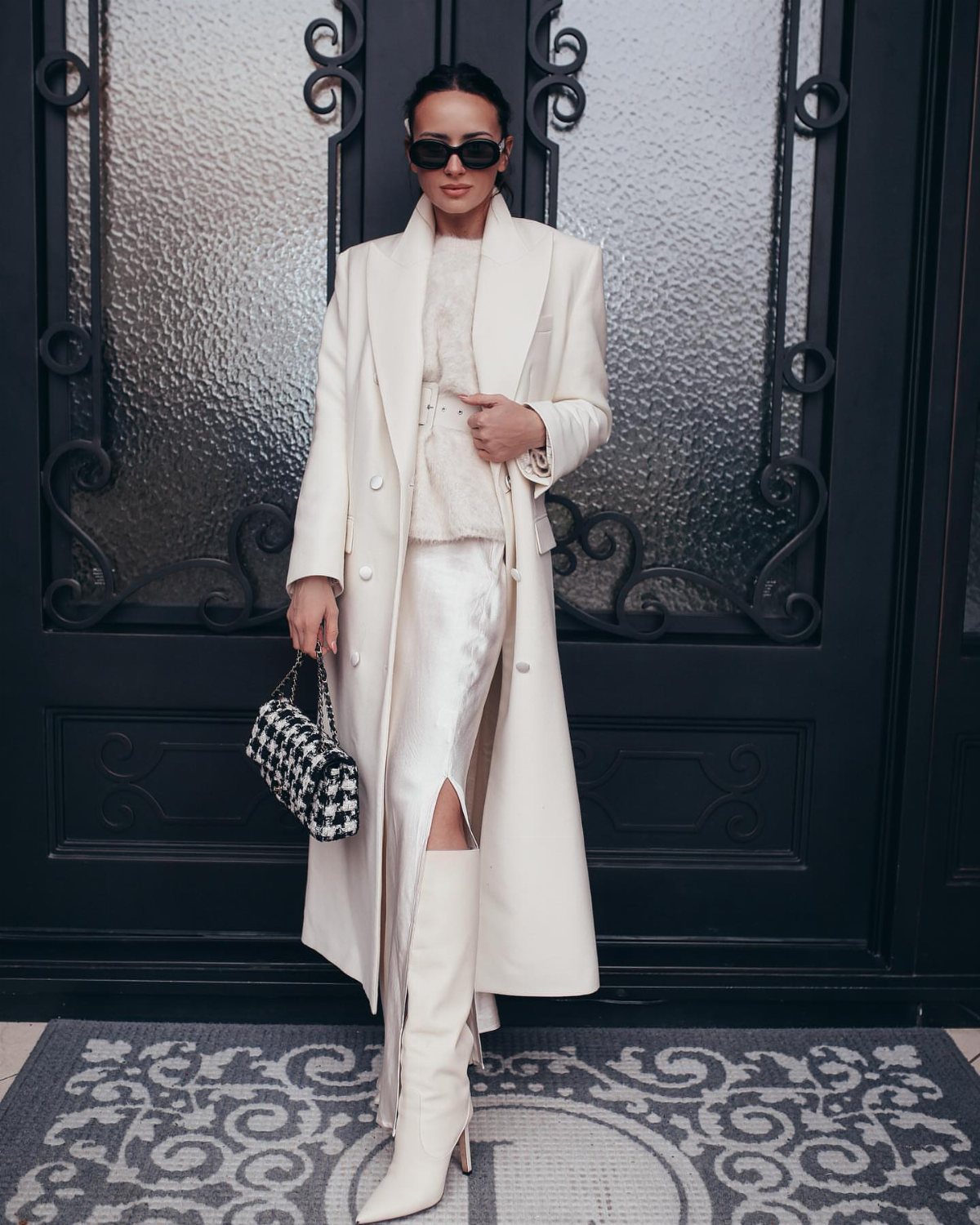Woman posing in an all-white winter outfit with a long coat and tall boots.