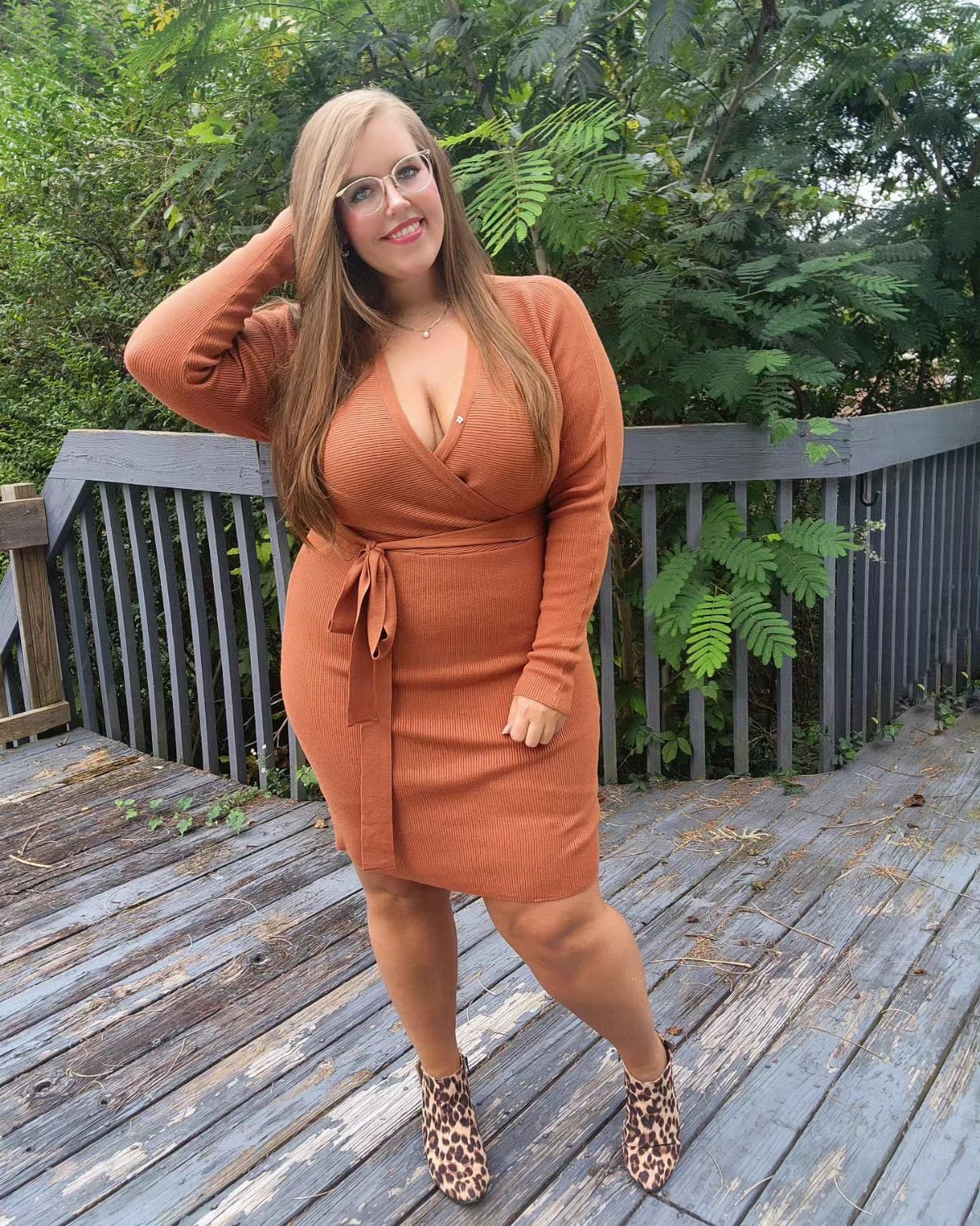 A woman in a burnt orange ribbed sweater dress and leopard print boots posing outdoors.