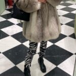 A person wearing a voluminous Arctic fox fur coat and zebra print leggings on a checkered floor.