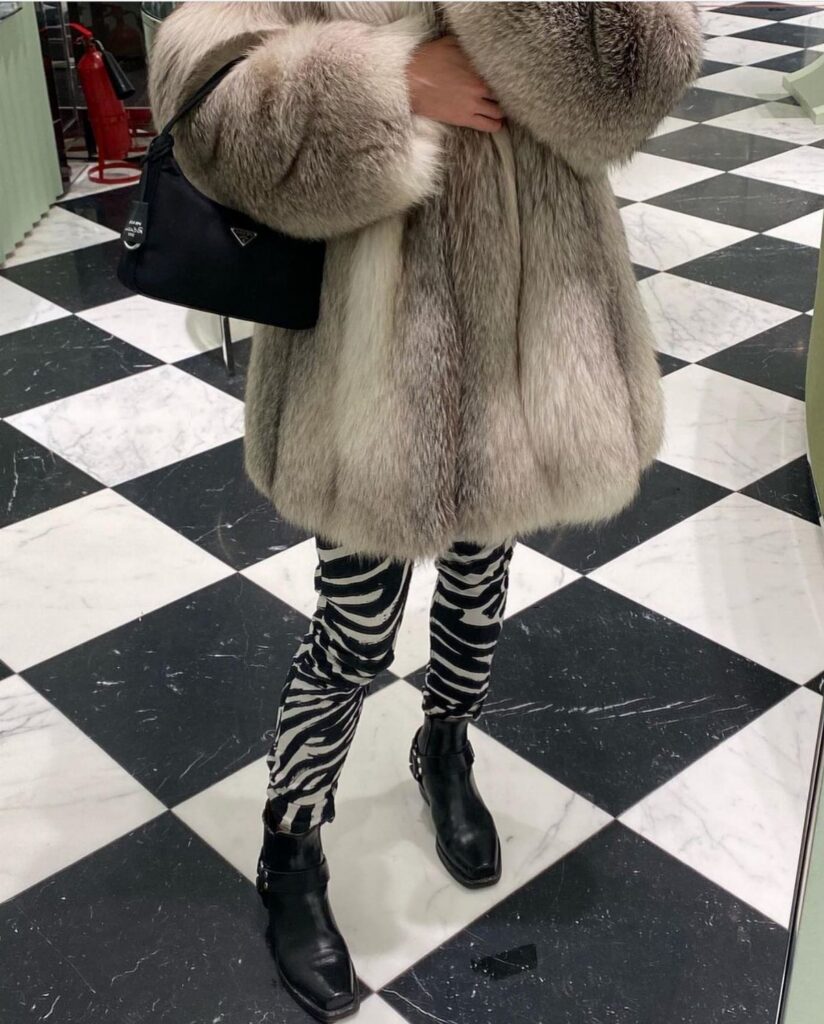 A person wearing a voluminous Arctic fox fur coat and zebra print leggings on a checkered floor.