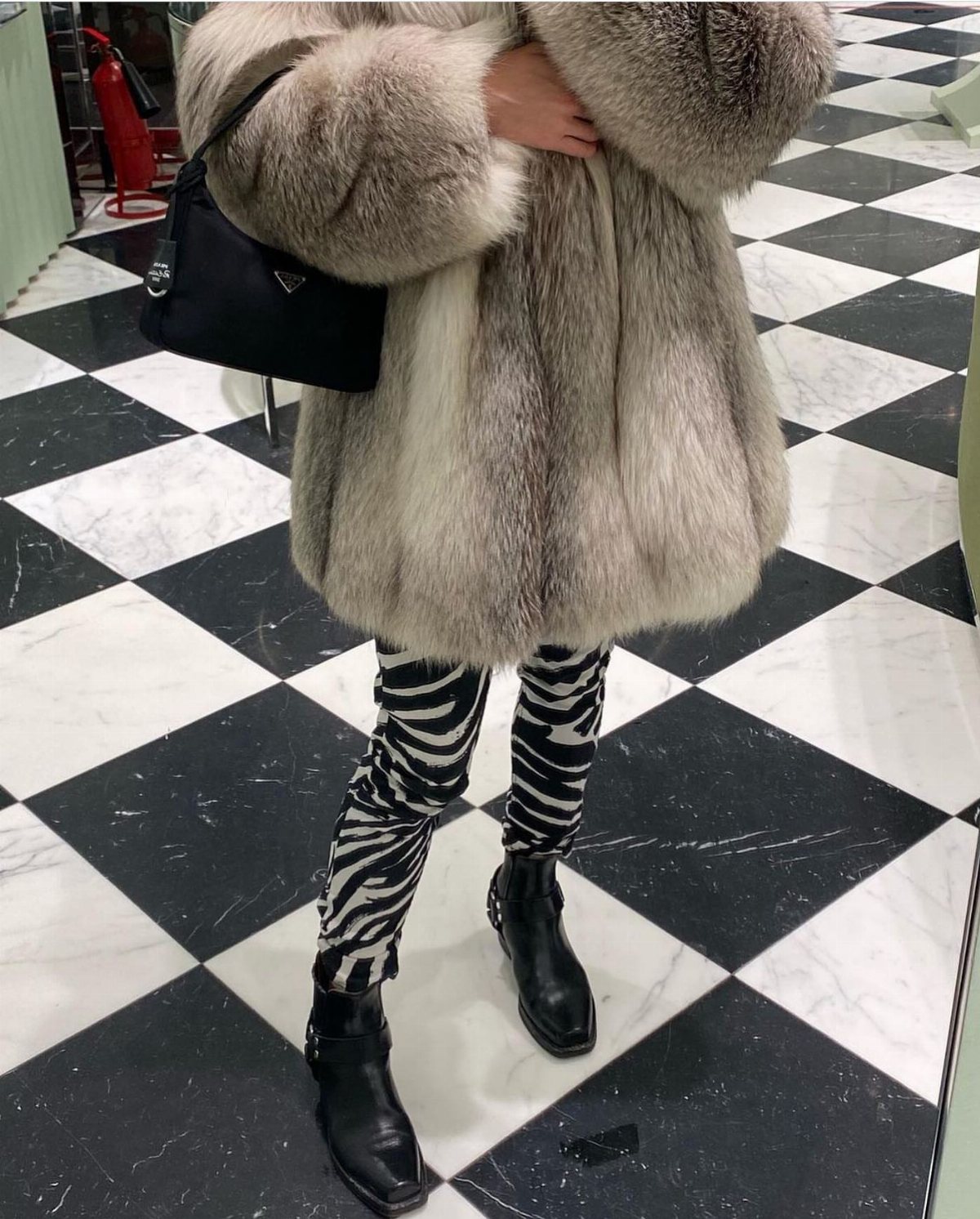 A person wearing a voluminous Arctic fox fur coat and zebra print leggings on a checkered floor.