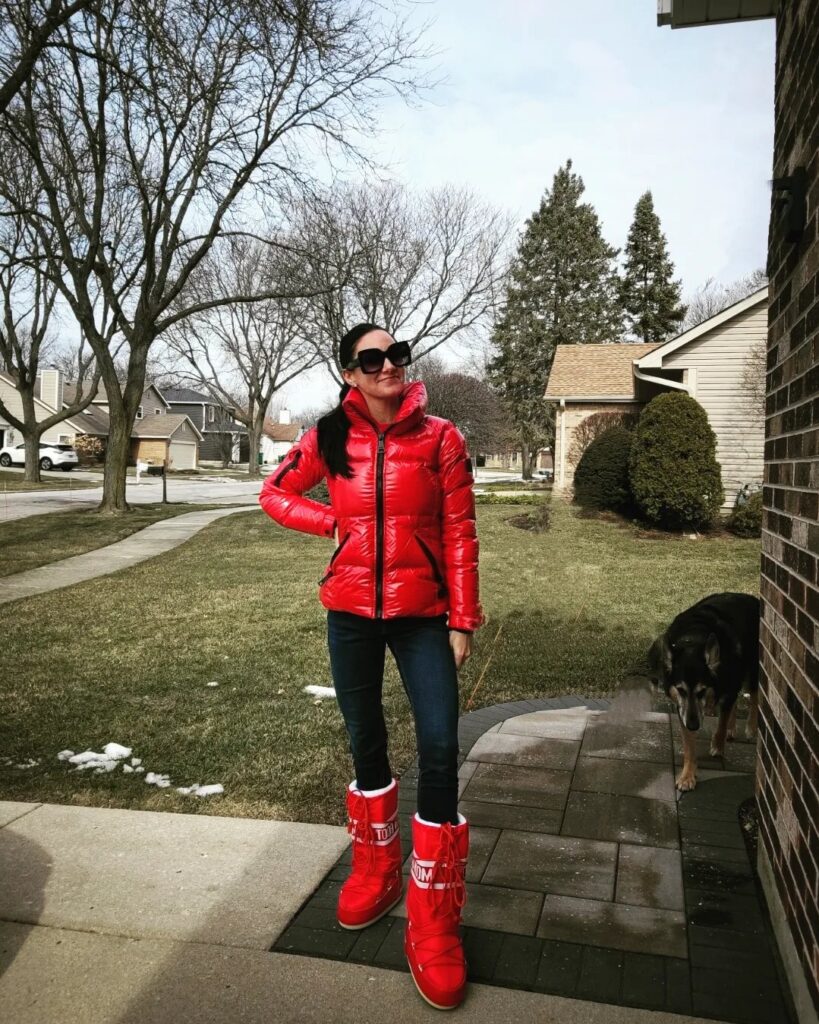 A woman in a bright red puffer jacket and red boots standing outdoors.