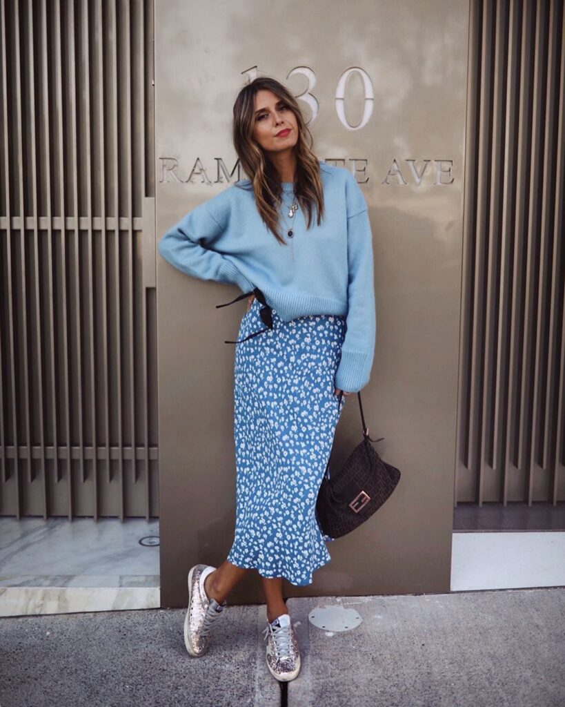 A woman wearing a light blue oversized knit sweater and a floral midi skirt.