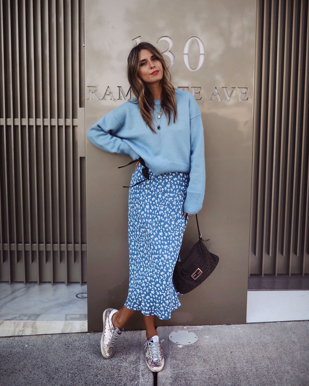A woman wearing a light blue oversized knit sweater and a floral midi skirt.