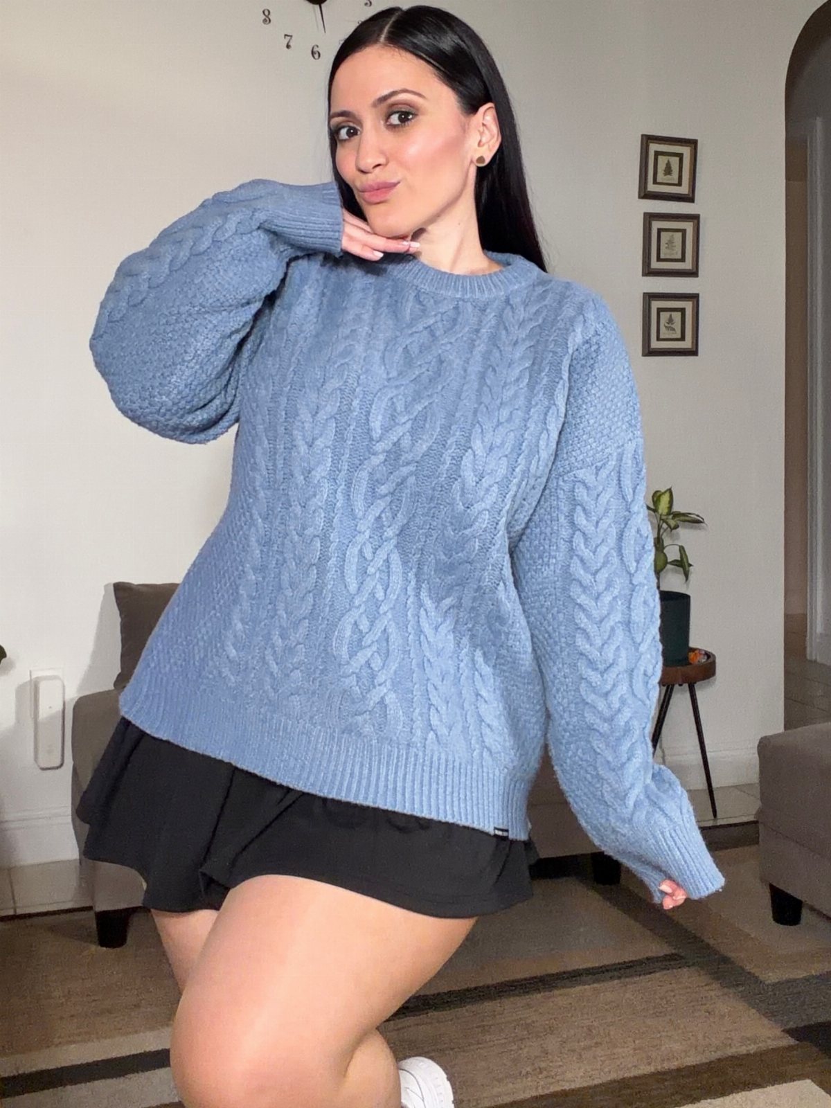 Woman posing in a light blue oversized cable-knit crewneck sweater and black skirt.