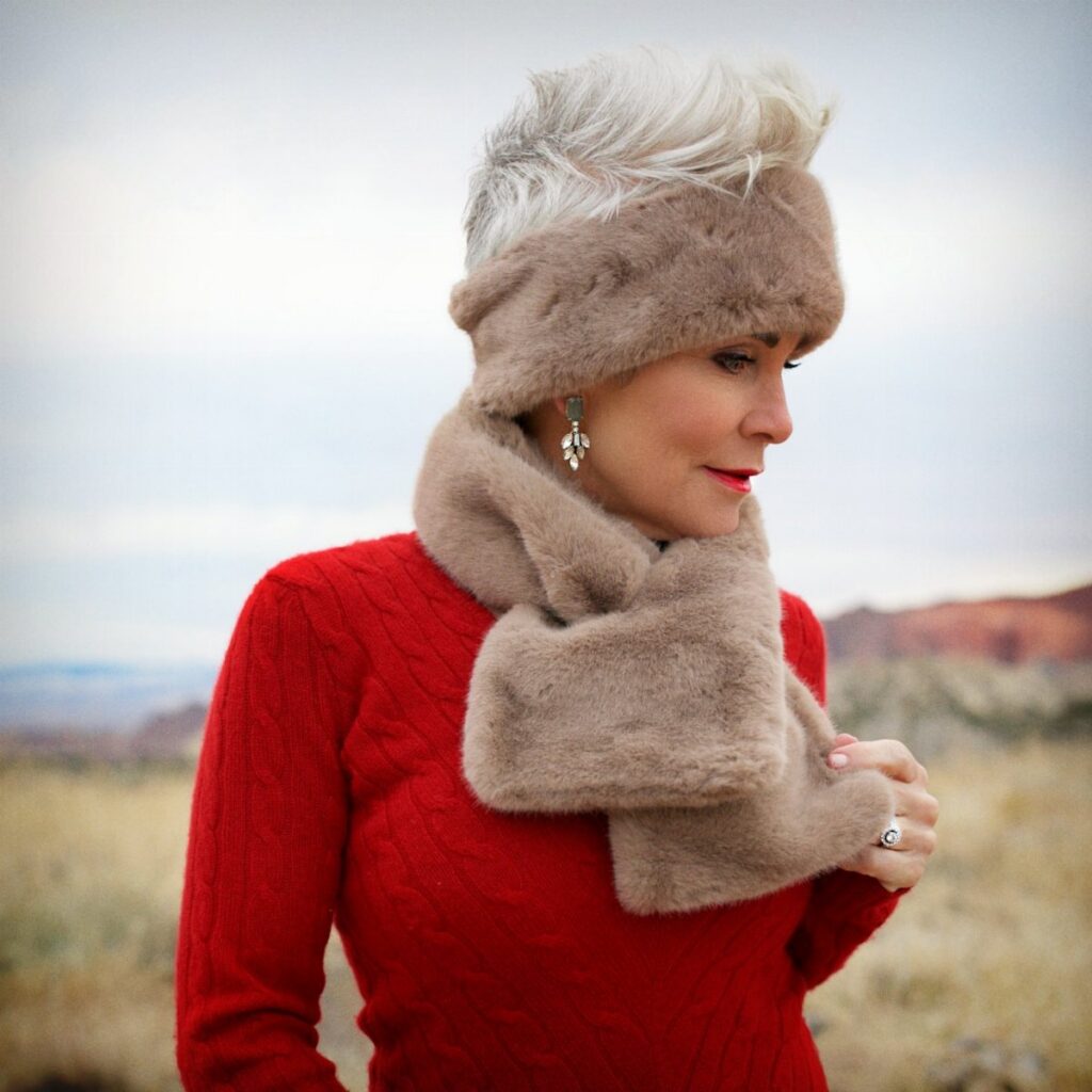 Woman in a red sweater wearing a tan faux fur headband and matching scarf outdoors.