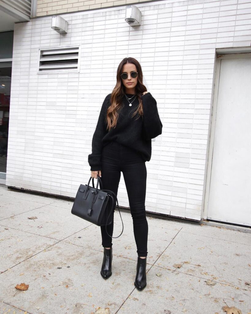 A woman dressed in an all-black outfit including black booties and a black handbag.