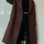 A person wearing a long brown double-breasted wool coat with black trousers.