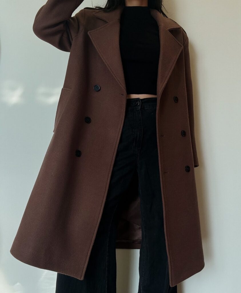 A person wearing a long brown double-breasted wool coat with black trousers.